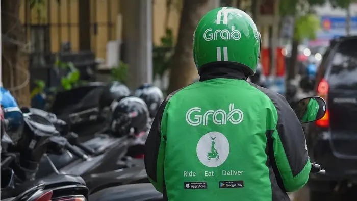 Seorang driver ojol dengan jaket dan helm hijau sedang berada di atas sepeda motor di tengah suasana jalan kota.