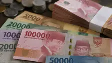 Sejumlah pecahan uang rupiah dan tumpukan uang kertas tampak tersusun di atas permukaan meja, disertai beberapa keping uang logam.