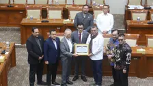 Foto memperlihatkan sesi foto bersama di ruang rapat Komisi III DPR RI, dengan latar belakang deretan meja dan kursi berwarna kayu cokelat khas ruang rapat parlemen. Delapan pria berdiri berjajar di barisan depan, sementara dua orang lainnya berdiri di barisan belakang.
