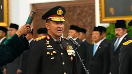 Komjen Pol. Suyudi Ario Seto tampak mengenakan seragam kepolisian lengkap dengan berbagai tanda jasa dan lencana kehormatan, berdiri di hadapan tangga berlatar merah sambil memberi hormat.