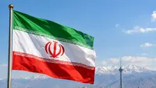 Bendera nasional Iran berkibar dengan latar panorama Kota Teheran dan pegunungan Alborz. Visual ini merepresentasikan posisi geografis Iran serta pernyataan Presiden Masoud Pezeshkian mengenai peluang kerja sama ekonomi dan perdagangan dengan negara-negara tetangga di tengah pembatasan yang diberlakukan Amerika Serikat.