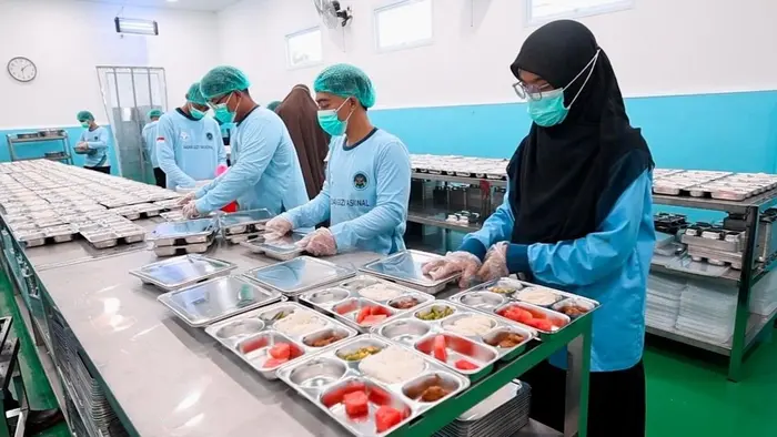 Pekerja dapur menyiapkan makanan dalam jumlah besar sebagai bagian dari program pemenuhan gizi