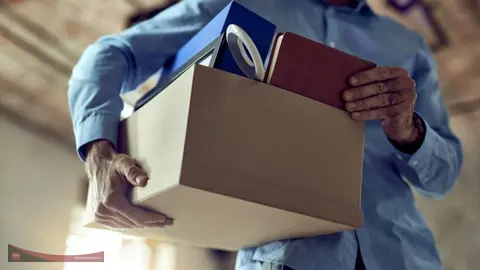 Foto ilustrasi ini menggambarkan seorang karyawan yang membawa kardus berisi barang-barang pribadinya seperti buku, bingkai foto, dan berkas kerja usai terkena pemutusan hubungan kerja (PHK).