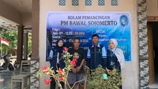Tiga mahasiswa KKN MIT UIN Walisongo Posko 168 berseragam biru berfoto bersama Yosi pemilik Kolam Pemancingan PM Bawal Sojomerto di depan banner promosi usaha yang baru dipasang.