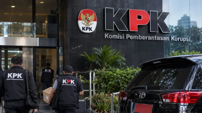 Foto ilustrasi jurnalistik menampilkan gedung Komisi Pemberantasan Korupsi (KPK) sebagai simbol proses penyidikan dugaan korupsi. Tampak petugas KPK membawa perlengkapan dan dokumen menuju gedung, dengan kendaraan di area depan. Foto menggambarkan aktivitas penggeledahan dan pendalaman perkara tanpa menampilkan tokoh yang terkait langsung dengan kasus.