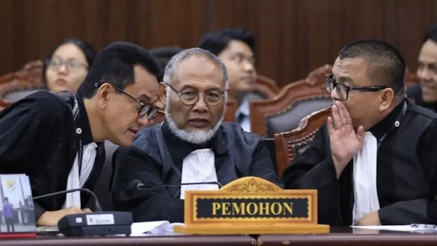 MK Tidak Temukan Bukti Ijazah Setara SMA Gibran Tiga pria berjubah hitam dengan kerah putih duduk berdekatan di belakang papan nama bertuliskan "PEMOHON". Pria di kiri dan kanan mencondongkan badan ke arah pria di tengah yang berkacamata dan berjenggot putih. Pria di kanan menutup mulutnya dengan tangan sambil berbisik. Di belakang mereka tampak kursi sidang dan beberapa orang lain.