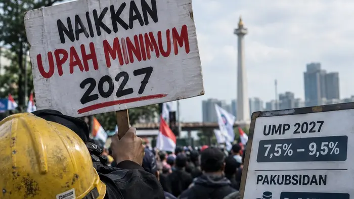 Ilustrasi jurnalistik menampilkan atribut pekerja dan suasana aksi buruh yang menyuarakan tuntutan kenaikan upah minimum 2027.